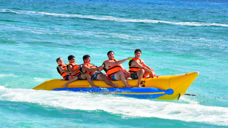 Five people on a yellow banana boat wearing life jackets in the sea.