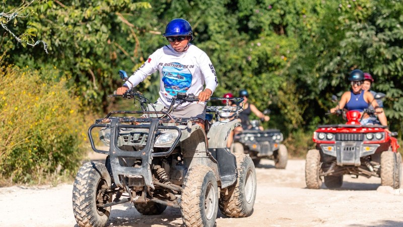 Group of people riding ATVs on a dirt path surrounded by trees.