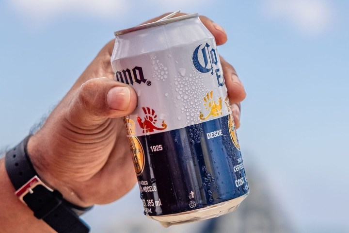 Hand holding a chilled beer can with drops, against a clear sky.