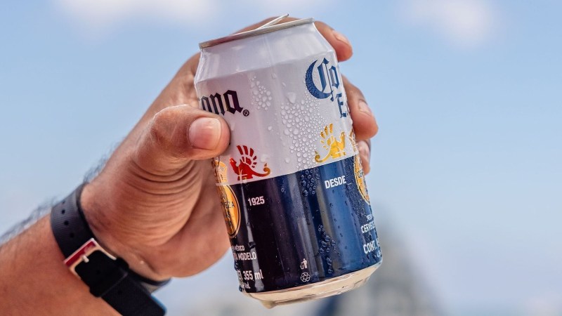 Hand holding a chilled beer can with drops, against a clear sky.