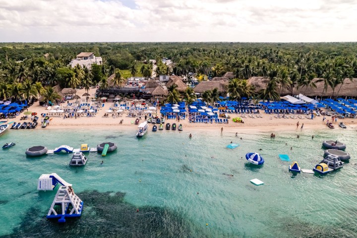 Aerial view of beach with umbrellas, loungers, and water inflatables in turquoise sea.