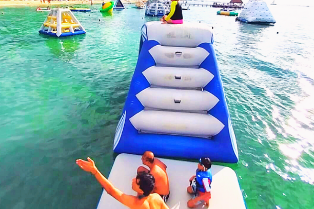 People on inflatable water obstacle course in the sea with beach in background.