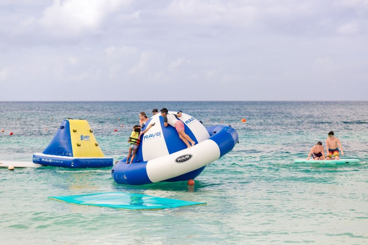 People playing on inflatable structures in the ocean on a cloudy day.