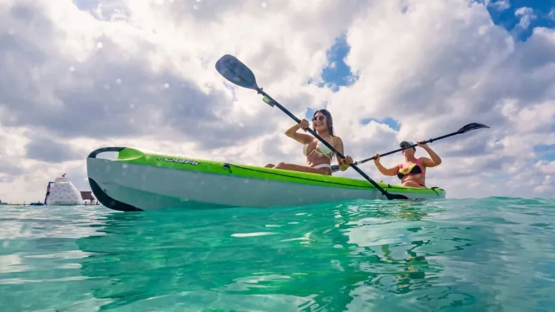 Two people kayaking on clear blue water under a cloudy sky.