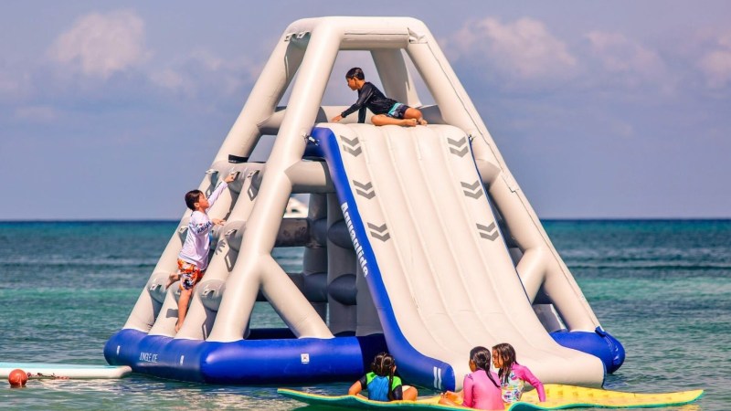 Kids playing on an inflatable water slide in the ocean.