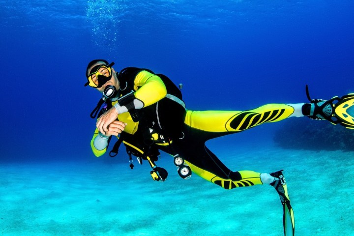 Diver in yellow suit and fins swimming underwater with scuba gear.