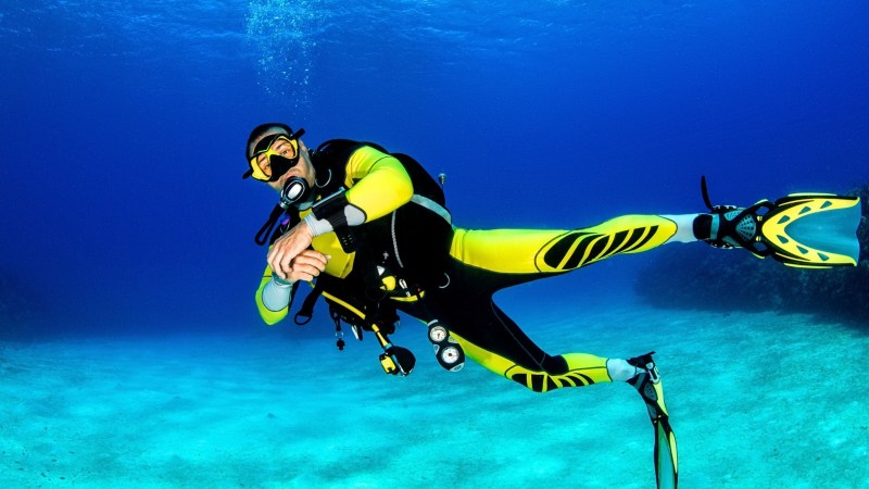 Diver in yellow suit and fins swimming underwater with scuba gear.