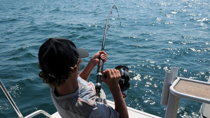 Person on a boat fishing, holding a fishing rod over the sparkling ocean.