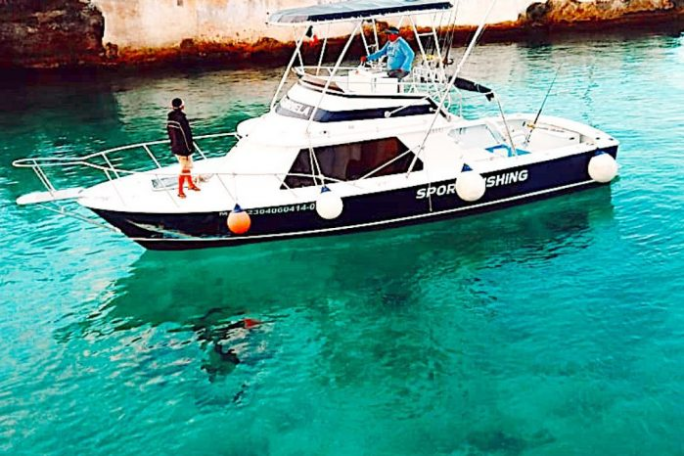 Boat on clear turquoise water with people on deck, diver visible underwater.