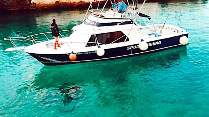 Boat on clear turquoise water with people on deck, diver visible underwater.