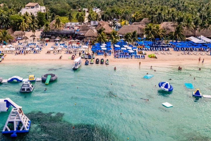 Aerial view of a beach with inflatables, loungers, umbrellas, and palm trees.
