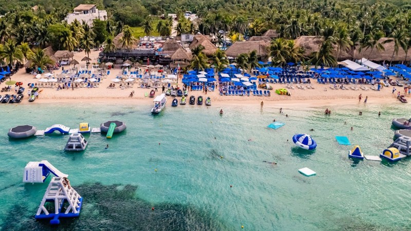 Aerial view of a beach with inflatables, loungers, umbrellas, and palm trees.