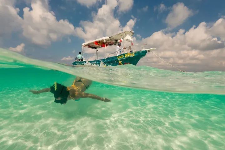 Person snorkeling underwater near a boat on a clear, sunny day.