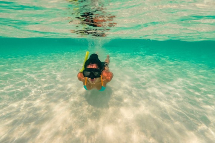 Underwater view of person snorkeling in clear turquoise water with sandy bottom.