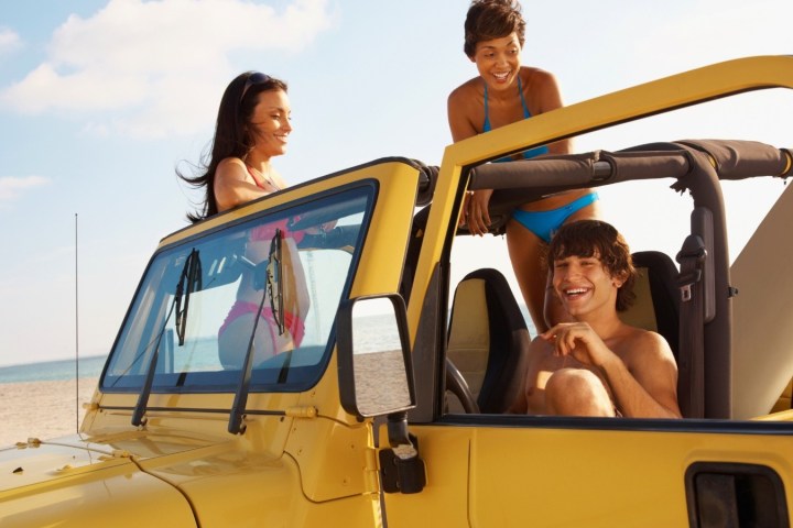 Three people laughing in a yellow Jeep on a beach.