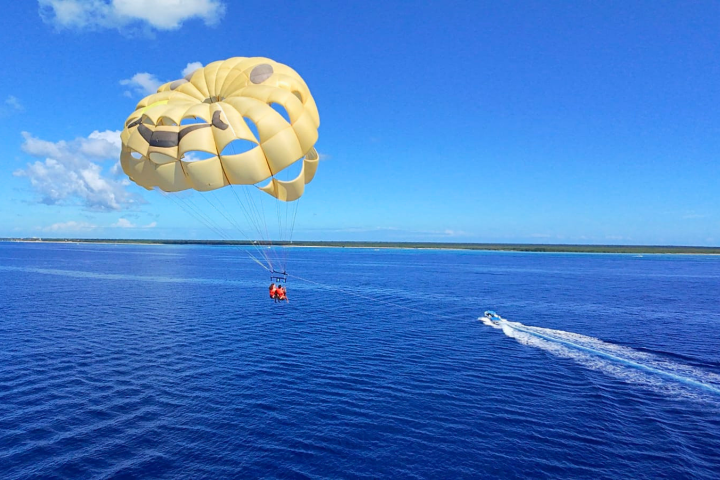 Parasailing over blue ocean with speedboat below and clear sky above.
