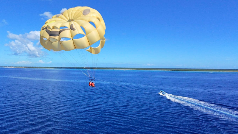 Parasailing over blue ocean with speedboat below and clear sky above.