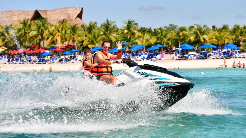 Two people on a jet ski near a tropical beach with palm trees.