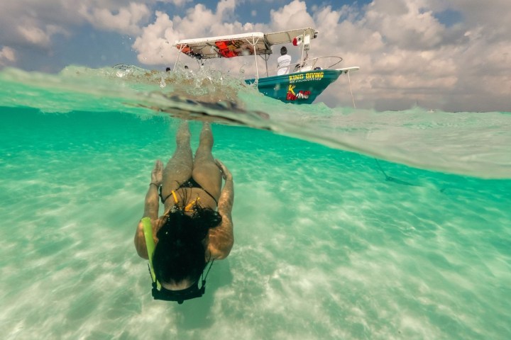 Person snorkeling underwater with boat above in clear turquoise sea.
