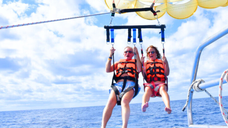 Two people parasailing with a yellow smiley face parachute over the ocean.
