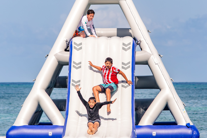Three kids playing on inflatable water slide at the beach.