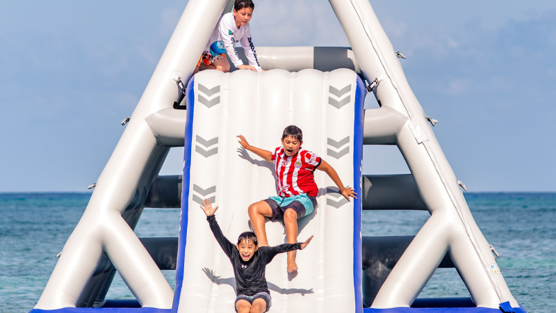 Three kids playing on inflatable water slide at the beach.