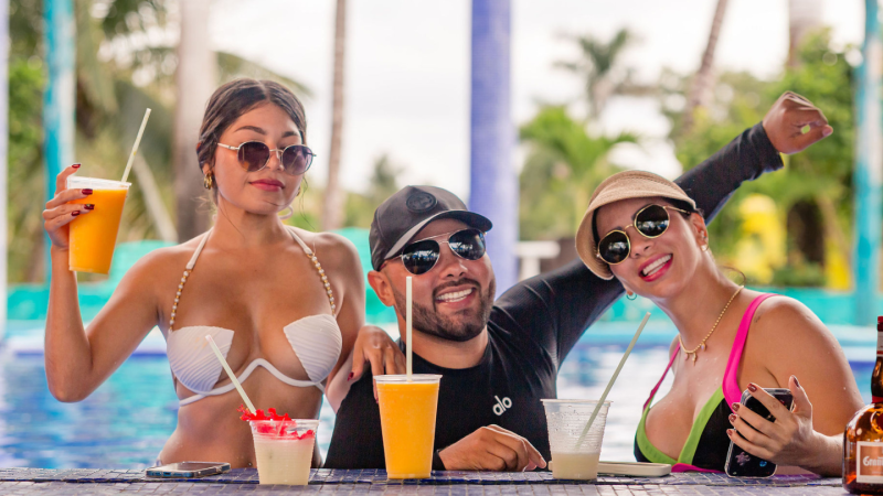 Three people in swimwear enjoy drinks in a poolside setting.