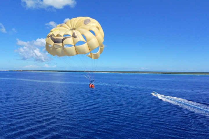 Parasailing over blue ocean with a yellow parachute and boat trailing a wake.
