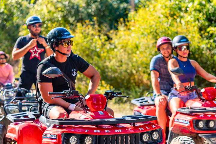 People riding red ATVs on a sunny day with trees in the background.