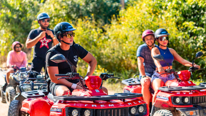 Group of people riding red ATVs through a forest trail, wearing helmets and sunglasses.
