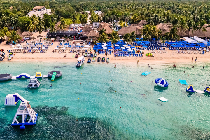 Aerial beach view with inflatable water park and sunbathers.