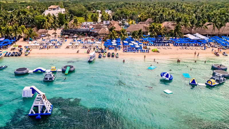 Aerial beach view with inflatable water park and sunbathers.