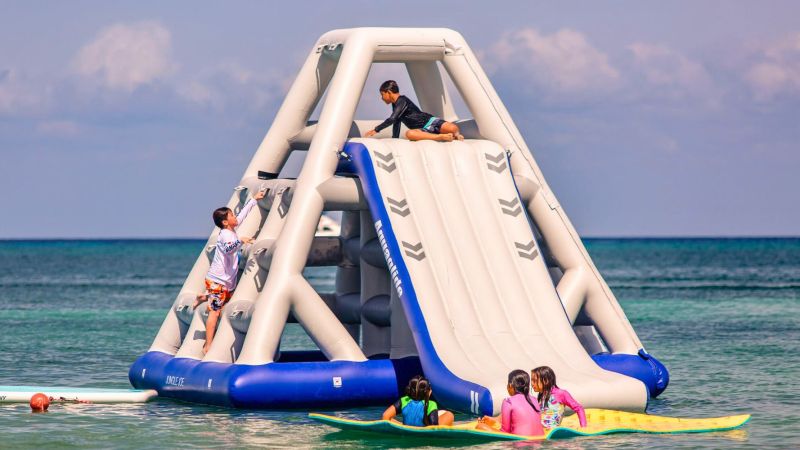 Kids playing on an inflatable climbing structure in the ocean.