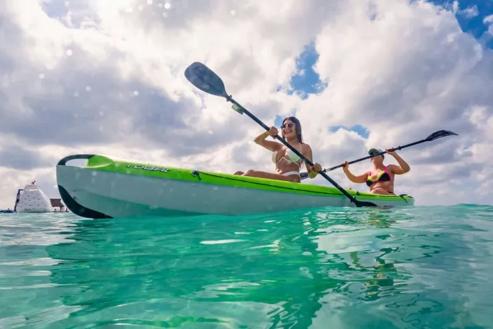 Two people kayaking in clear turquoise water under a cloudy sky.