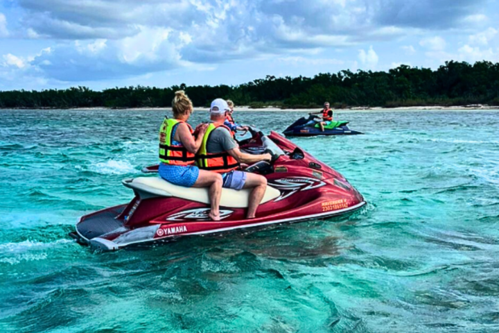 People riding jet skis in clear turquoise water near a forested shoreline.