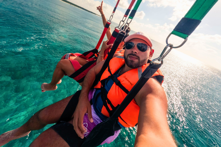 Two people parasailing over the ocean with life vests and harnesses.