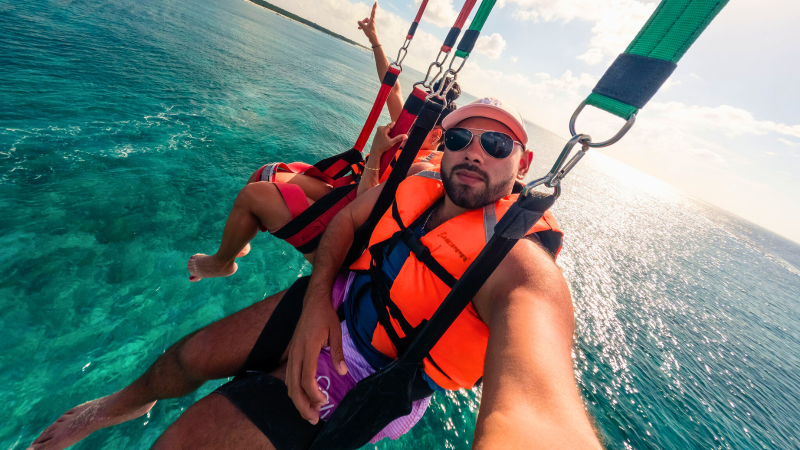 Two people parasailing over the ocean with life vests and harnesses.