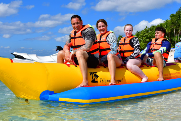 Four people on a yellow inflatable banana boat on the water, wearing life jackets.