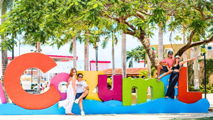Four people pose by colorful Cozumel sign with trees in the background.